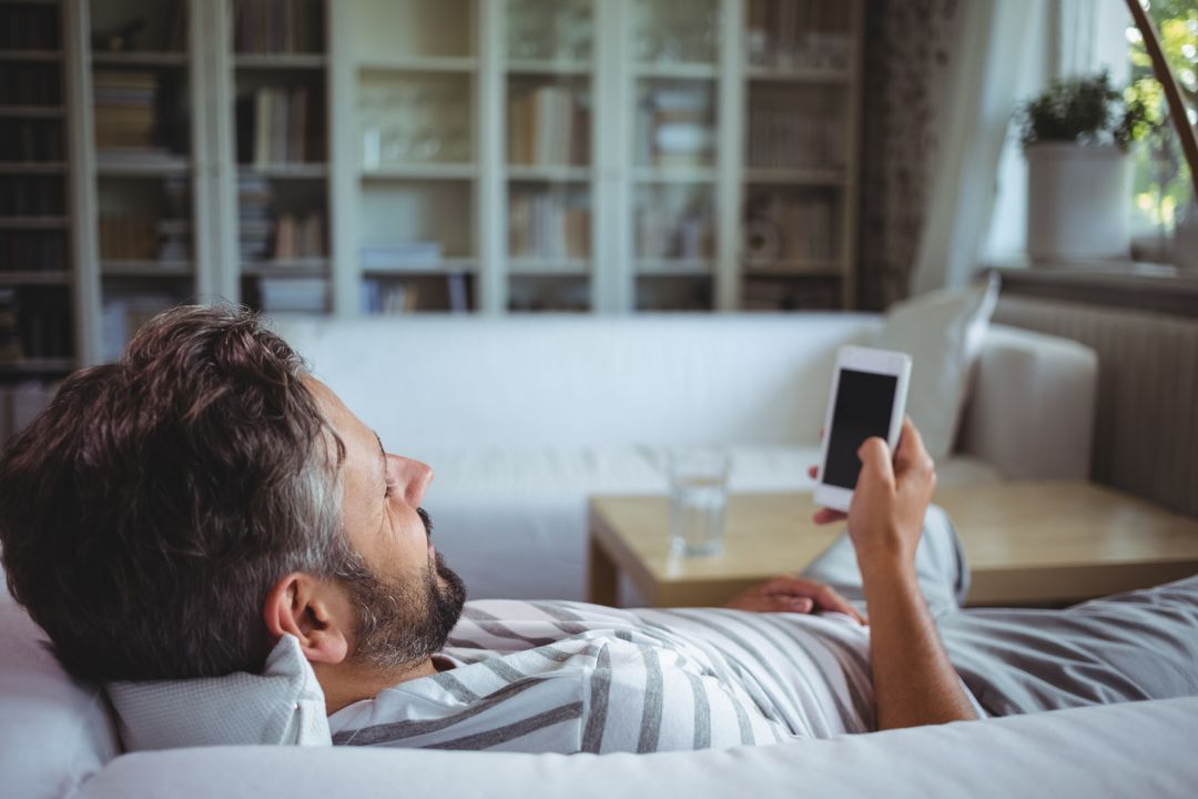 Man Relaxing on Couch Using Smartphone in Cozy Living Room - Free Images, Stock Photos and Pictures on Pikwizard.com