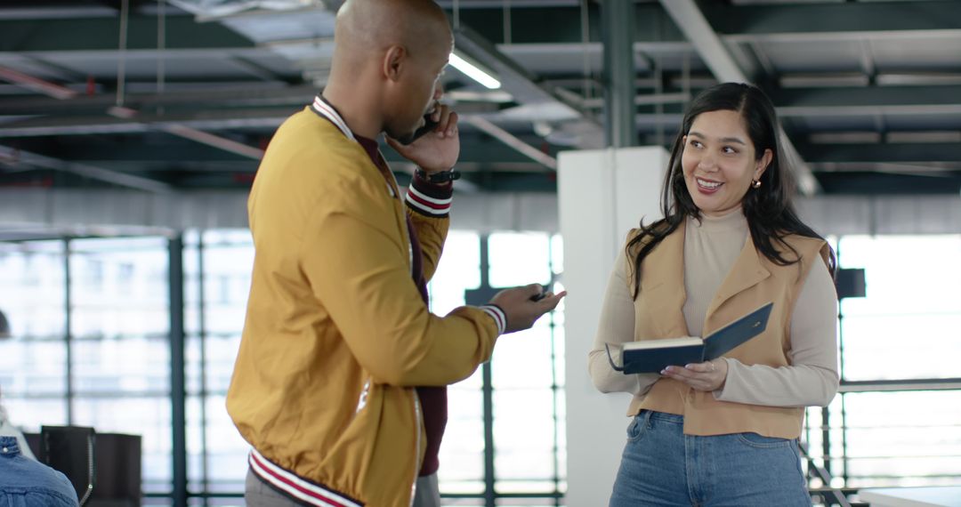 Diverse coworkers collaborating in modern office holding notebook and talking on phone