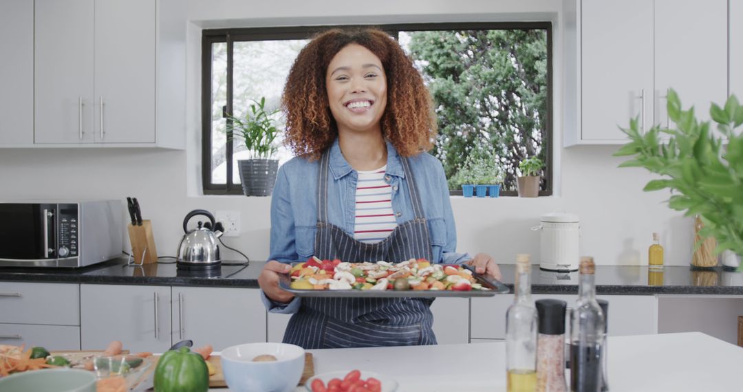 Smiling Woman Holding Tray of Vegetables in Modern Kitchen - Free Images, Stock Photos and Pictures on Pikwizard.com