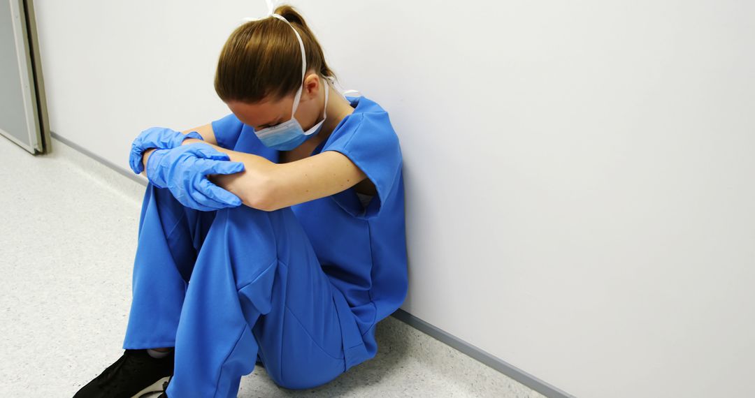 Exhausted Healthcare Worker in PPE Sitting Against Wall - Free Images, Stock Photos and Pictures on Pikwizard.com