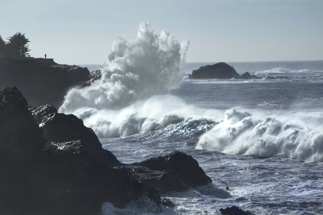 Massive Waves Crashing on Rugged Coastline with Lone Silhouette on Clifftop