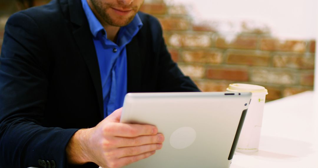 Businessman Focusing on Tablet with Coffee at Modern Office - Free Images, Stock Photos and Pictures on Pikwizard.com