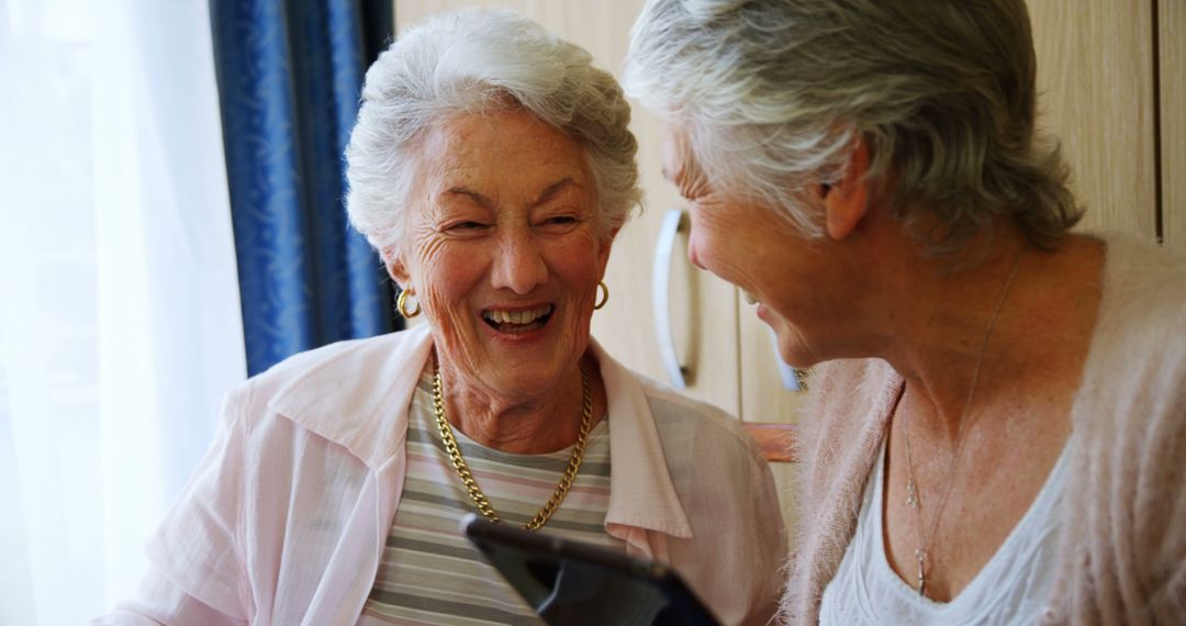 Senior women laughing together holding tablet - Free Images, Stock Photos and Pictures on Pikwizard.com