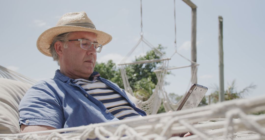 Relaxed Senior Man in Straw Hat Reading on Tablet in Hammock Outdoors - Free Images, Stock Photos and Pictures on Pikwizard.com