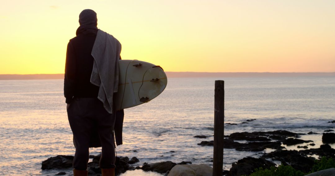 Surfer Watching Sunrise on Rocky Coastline Preparing for Surfing Session - Free Images, Stock Photos and Pictures on Pikwizard.com