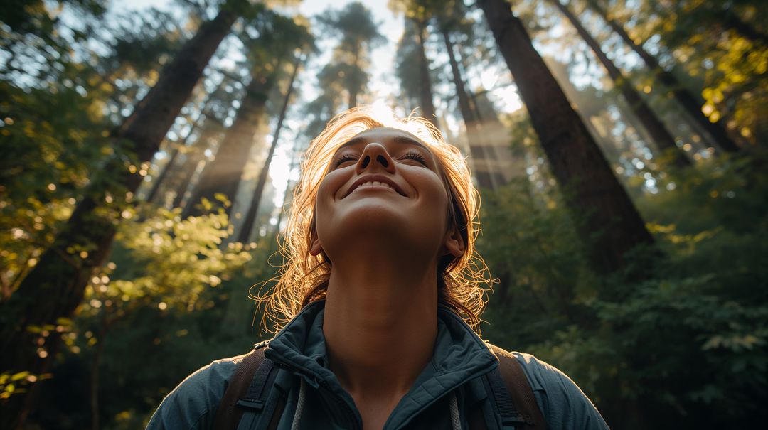 Sunlit hiker smiling upward amid towering conifers during golden hour forest walk