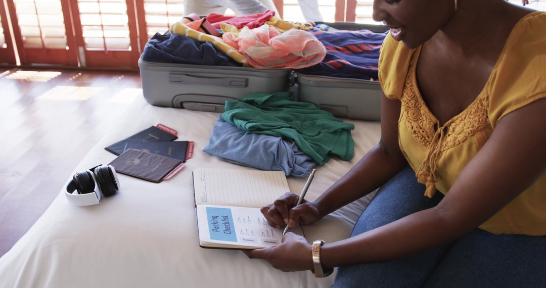 African American woman packing suitcase and writing travel checklist, planning vacation