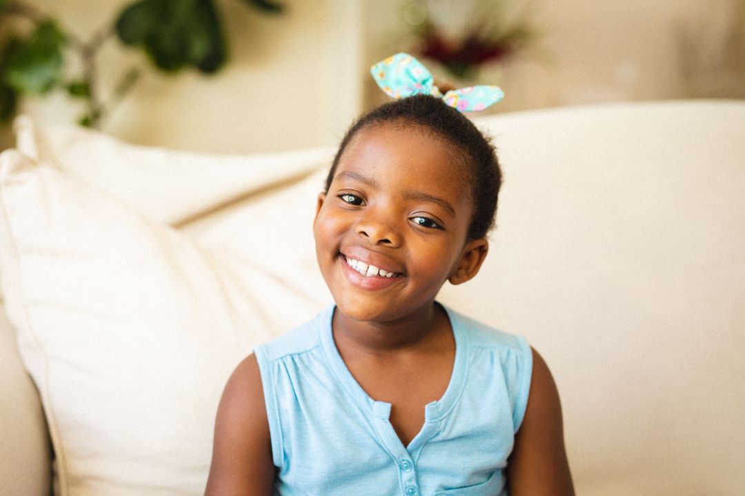 Portrait of smiling african american elementary girl sitting on sofa at home - Free Images, Stock Photos and Pictures on Pikwizard.com