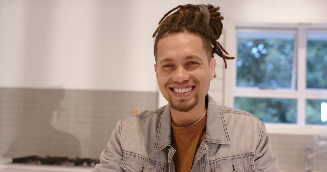 Smiling African American man leaning on kitchen counter in modern home wearing denim jacket