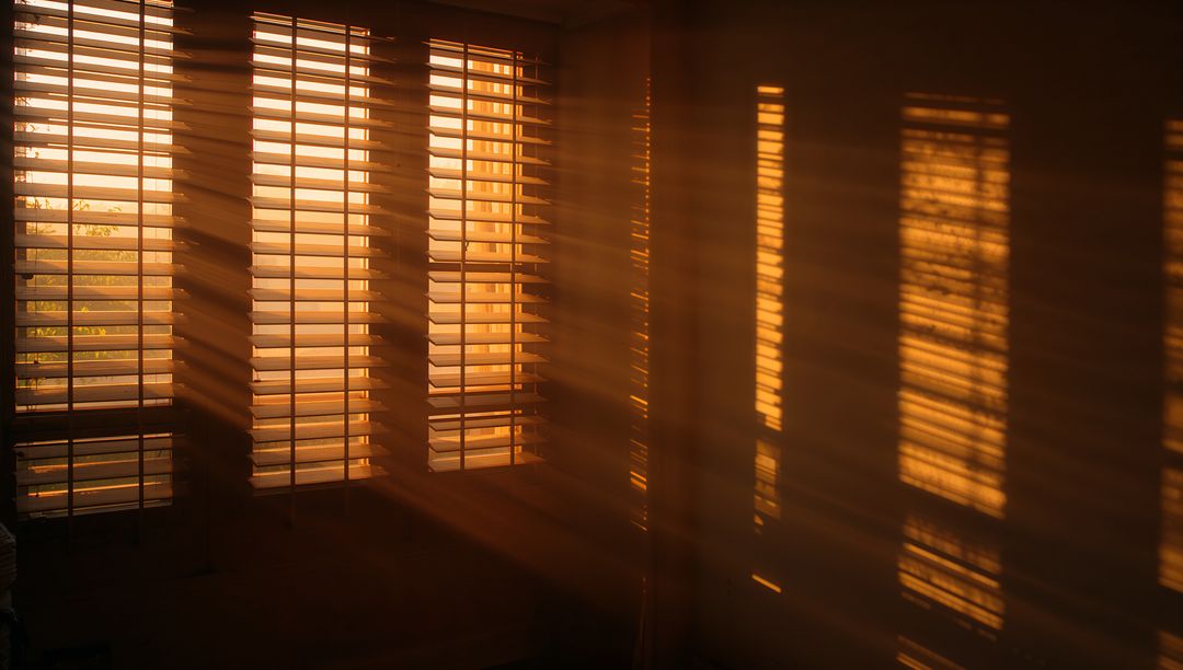 Golden sunlight streaming through slatted blinds casting warm striped shadows on interior