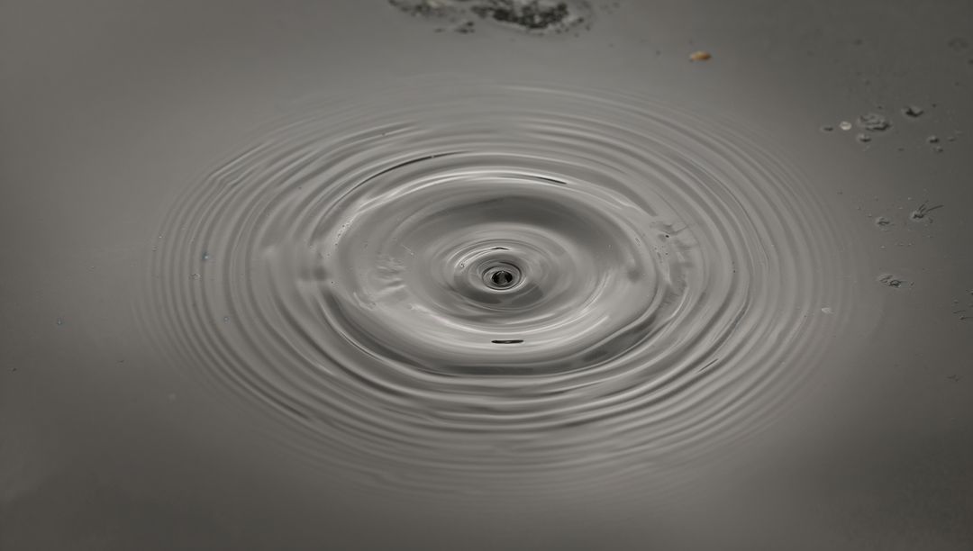 Monochrome water ripple forming central micro-whirlpool with concentric ripple rings