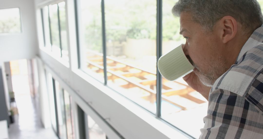 Man drinking coffee looking out bright modern home windows - Free Images, Stock Photos and Pictures on Pikwizard.com