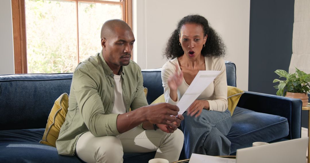 Diverse Couple Analyzing Financial Document on Couch