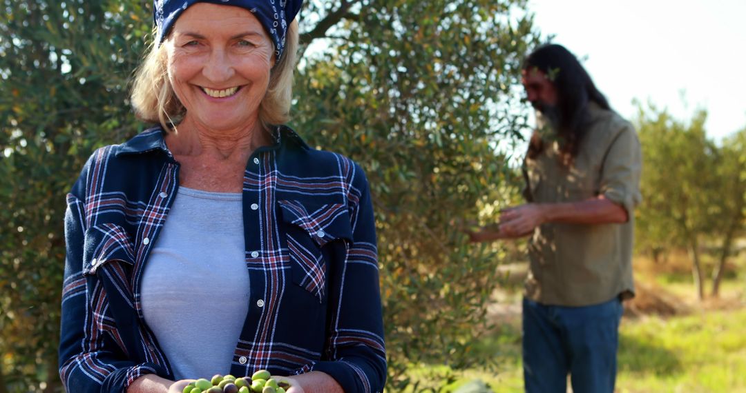 Happy Woman Harvesting Olives in Orchard with Colleague in Background - Free Images, Stock Photos and Pictures on Pikwizard.com