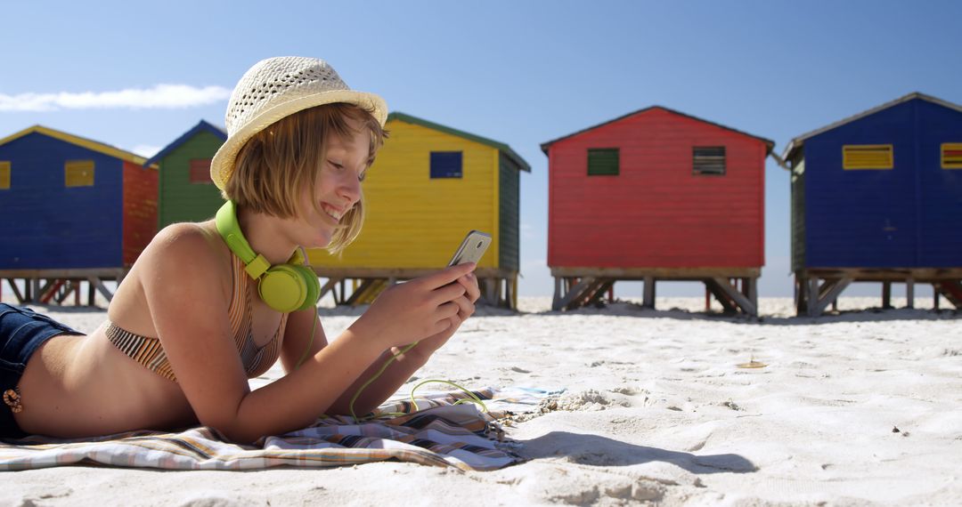 Smiling Girl with Headphones Relaxing on Beach by Colorful Beach Huts - Free Images, Stock Photos and Pictures on Pikwizard.com