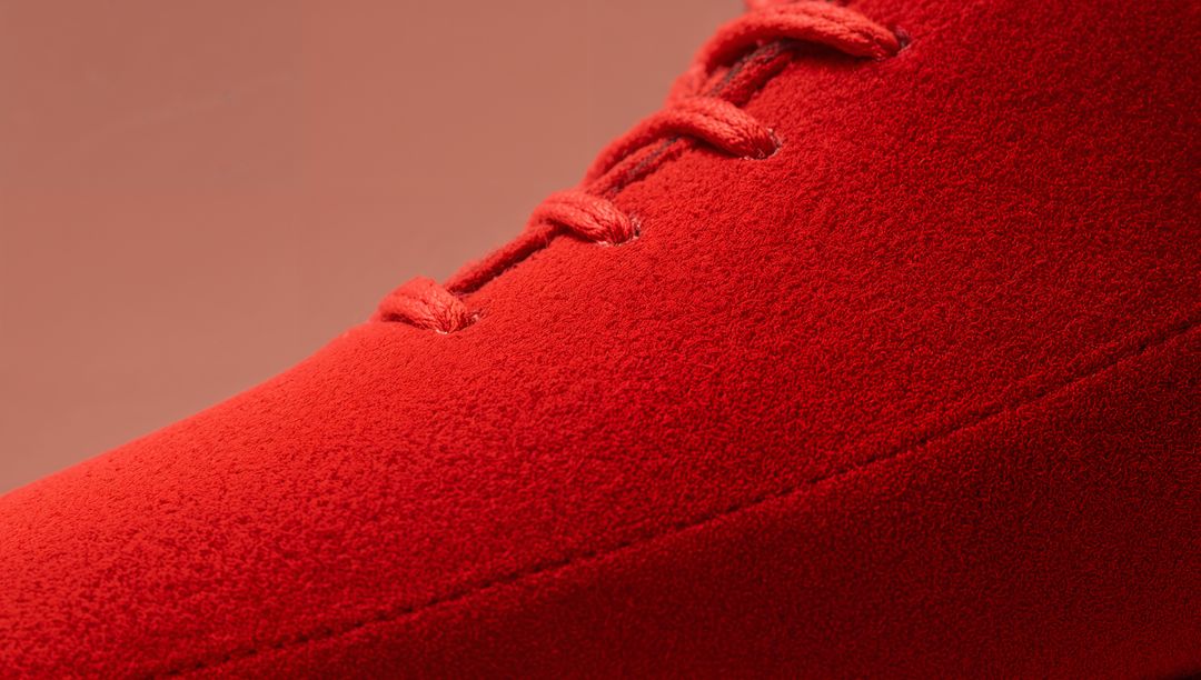 Close-up Red Suede Shoe Upper Showing Laces, Diagonal Seam and Soft Nap Texture on Studio Backdrop