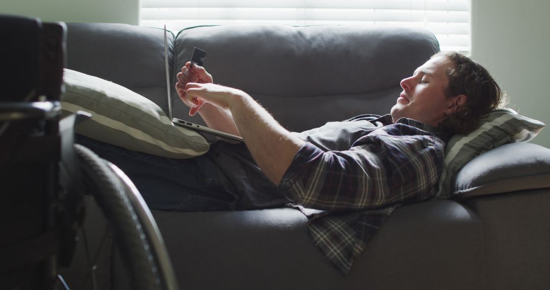 Man Lying on Sofa Using Phone Next to Wheelchair - Free Images, Stock Photos and Pictures on Pikwizard.com