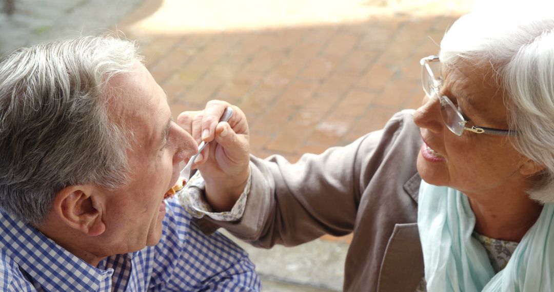 Senior Woman Feeding Elderly Man Outdoors on Sunny Day - Free Images, Stock Photos and Pictures on Pikwizard.com