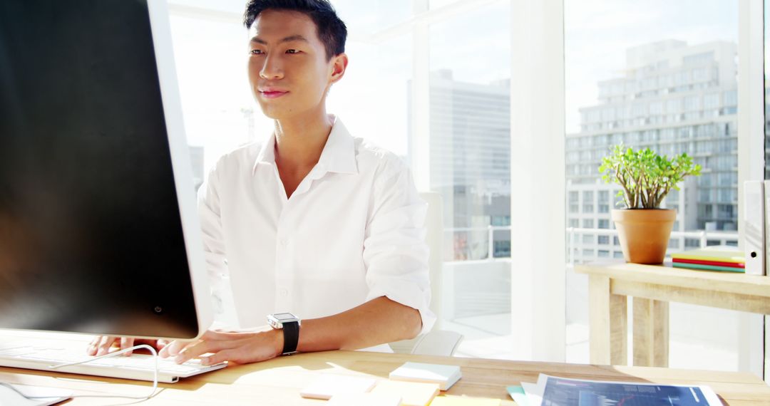 Asian Man Working on Desktop Computer in Bright Office - Free Images, Stock Photos and Pictures on Pikwizard.com