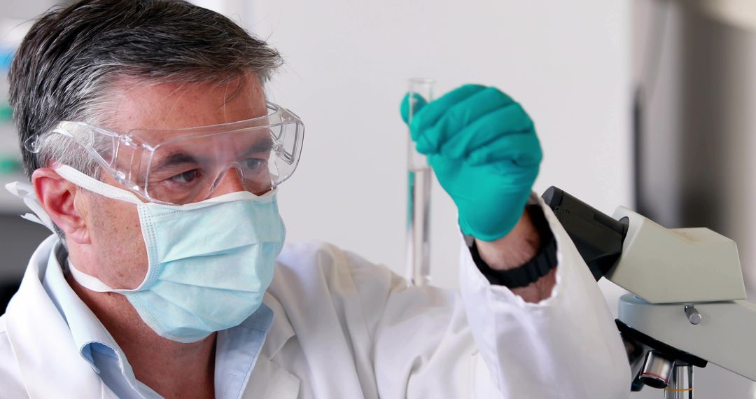 Laboratory researcher inspecting test tube wearing PPE at microscope in clinical lab