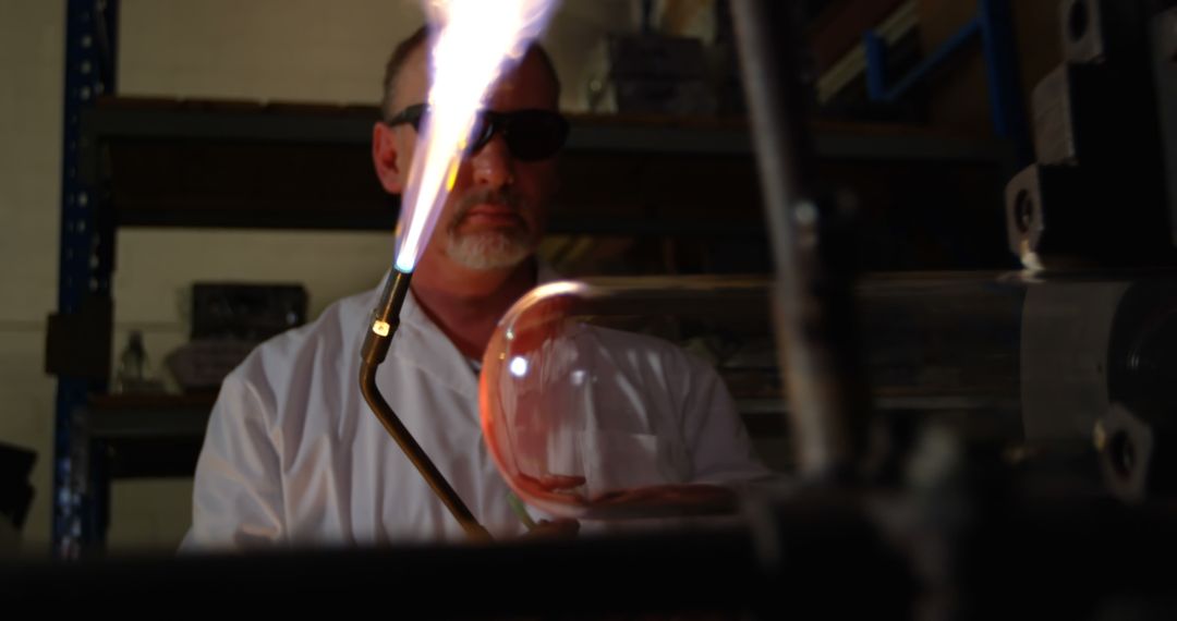 Glassblower shaping molten glass with torch in workshop - Free Images, Stock Photos and Pictures on Pikwizard.com