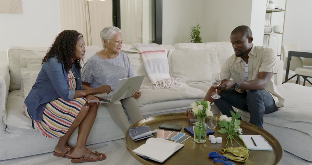 Multigenerational multiracial family sitting on beige sofa consulting color swatches with laptop