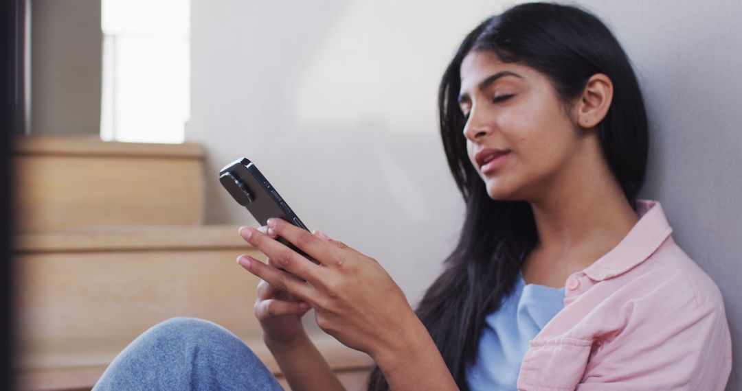 Young woman leaning on wall using smartphone indoors - Free Images, Stock Photos and Pictures on Pikwizard.com