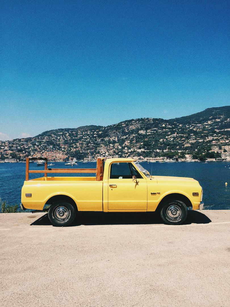 Vintage yellow pickup truck by the seaside with hills in the background - Free Images, Stock Photos and Pictures on Pikwizard.com