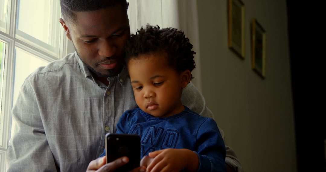 African American father and toddler using smartphone at home - Free Images, Stock Photos and Pictures on Pikwizard.com