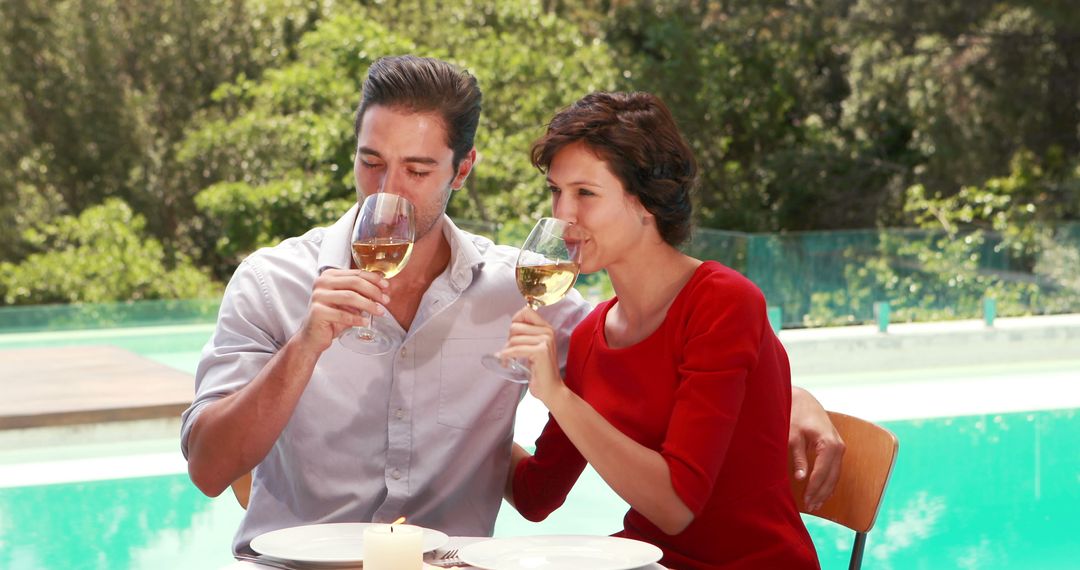 A Caucasian couple enjoys a romantic outdoor meal by a pool, toasting with glasses of white wine - Free Images, Stock Photos and Pictures on Pikwizard.com