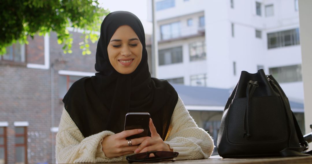 Smiling Woman in Hijab Using Smartphone Outdoors on Sunny Day - Free Images, Stock Photos and Pictures on Pikwizard.com