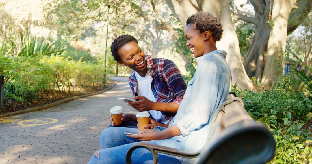 Happy Twin Sisters Laughing and Enjoying Coffee in Park