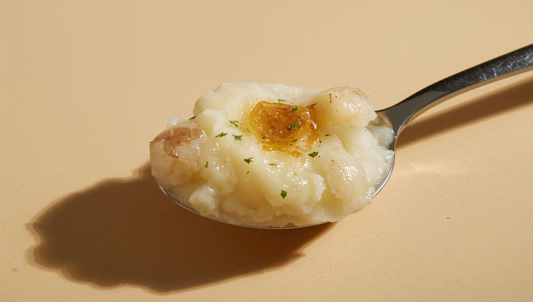 Spoonful of creamy mashed potato with melting butter and parsley garnish on beige surface