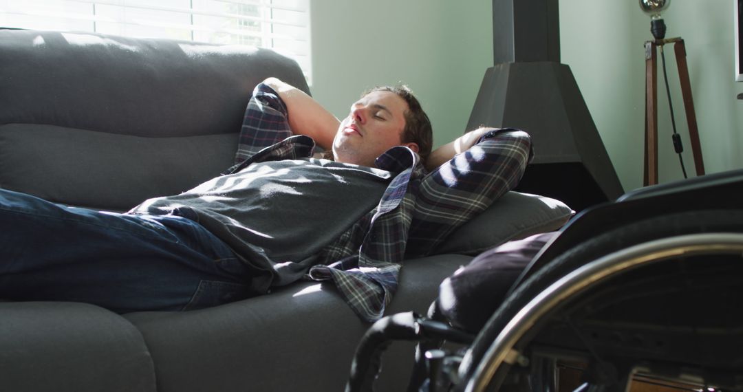 Man Relaxing on Couch with Wheelchair Nearby in Bright Living Room - Free Images, Stock Photos and Pictures on Pikwizard.com