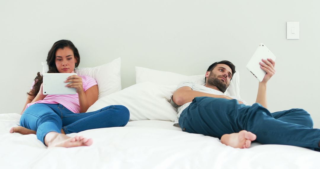Couple Relaxing in Bedroom Using Tablets for Leisure