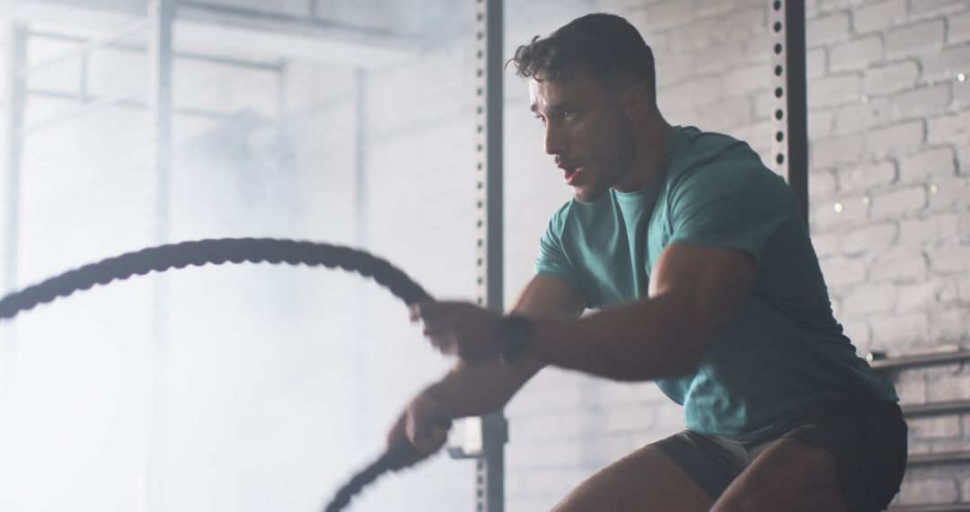 Determined Athlete Training with Battle Ropes in Gym