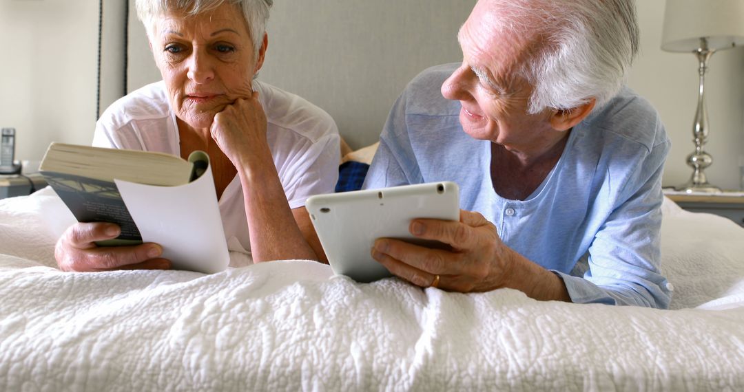 Senior Couple Engaging with Technology and Reading on Bed