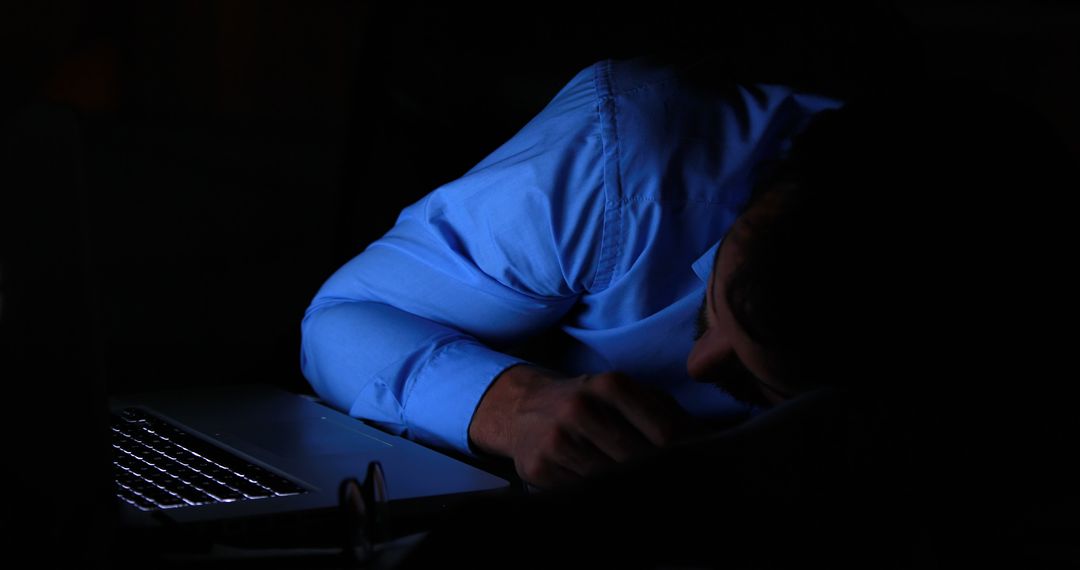 Exhausted Man Sleeping on Desk Next to Laptop in Dim Light - Free Images, Stock Photos and Pictures on Pikwizard.com