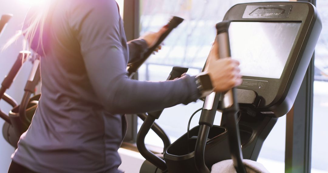 Person Using Elliptical Trainer in Modern Gym with Sunlight - Free Images, Stock Photos and Pictures on Pikwizard.com