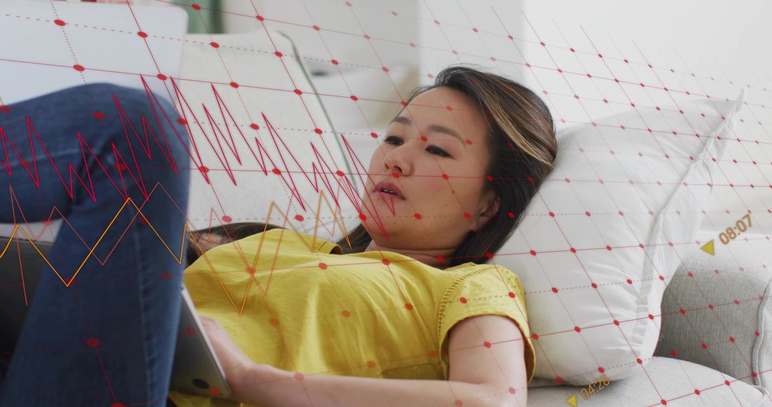 Reclining Korean woman using tablet on sofa with red data grid overlay suggesting analytics and calm