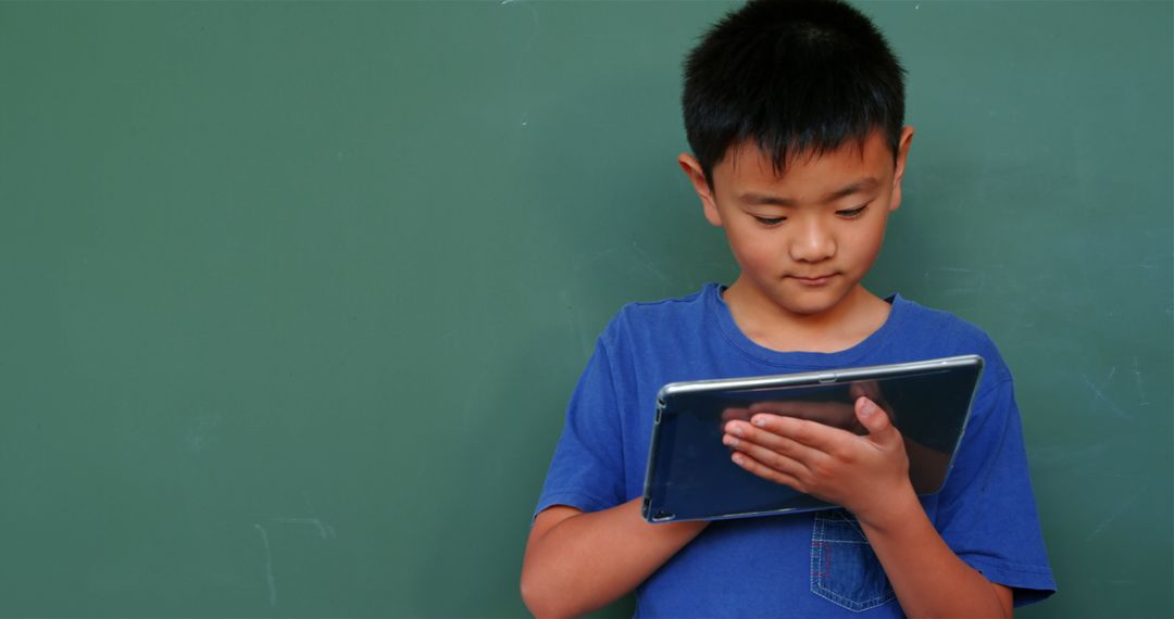 Focused Schoolboy Using Tablet Against Green Chalkboard