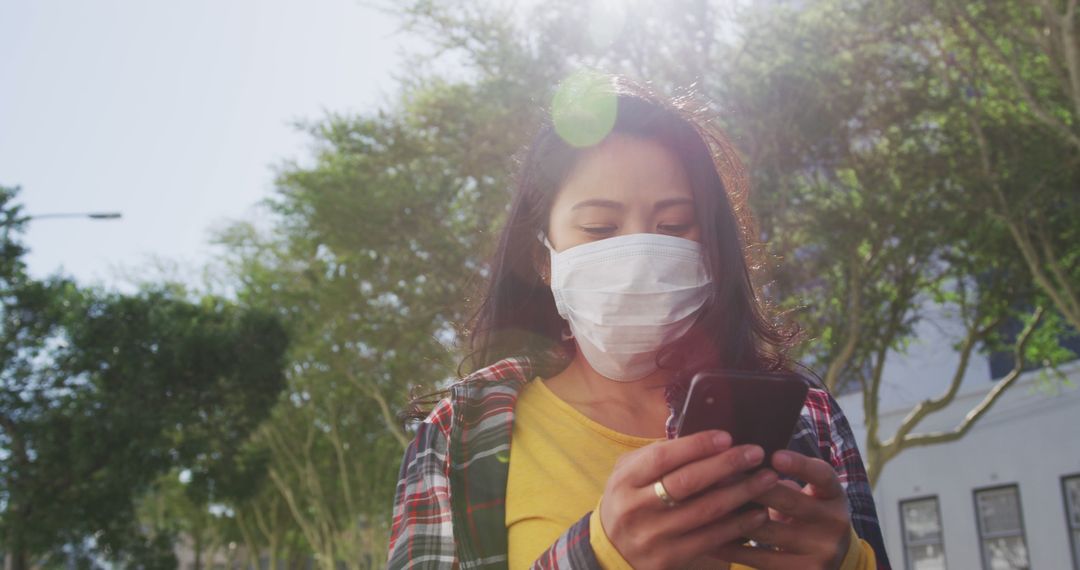 Young woman wearing mask using smartphone outdoors on sunny day - Free Images, Stock Photos and Pictures on Pikwizard.com