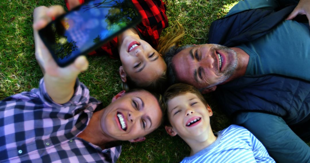 Happy family lying on grass taking selfie outdoors - Free Images, Stock Photos and Pictures on Pikwizard.com