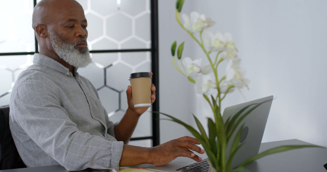 Mature Man Drinking Coffee and Using Laptop in Modern Office - Free Images, Stock Photos and Pictures on Pikwizard.com