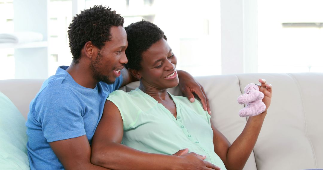 Expectant Couple Sitting on Couch Holding Baby Shoes Smiling - Free Images, Stock Photos and Pictures on Pikwizard.com