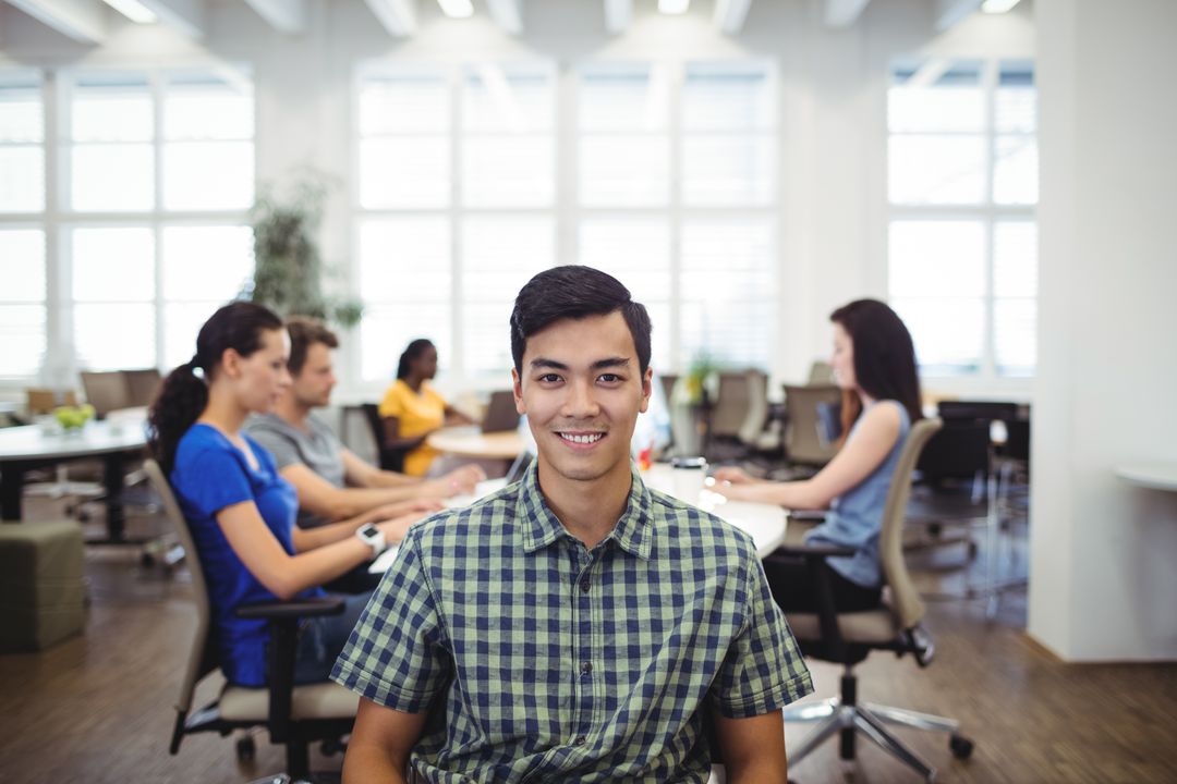 Smiling Businessman in Office with Colleagues in Background