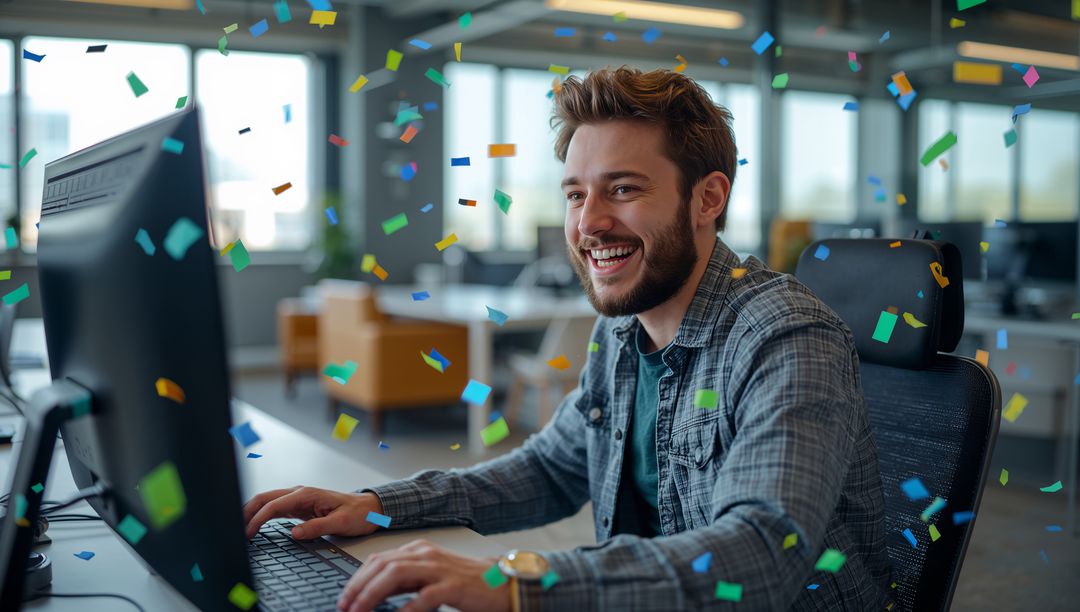 Smiling man celebrating at desk with colorful confetti in modern open-plan office