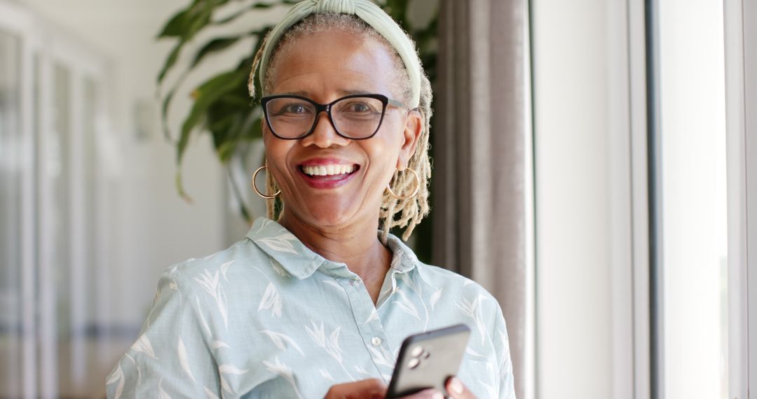 Smiling Senior Woman with Smartphone by Window