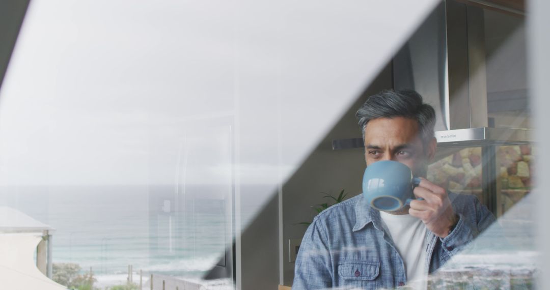 Middle-aged Man Drinking Coffee by Window Overlooking Ocean - Free Images, Stock Photos and Pictures on Pikwizard.com