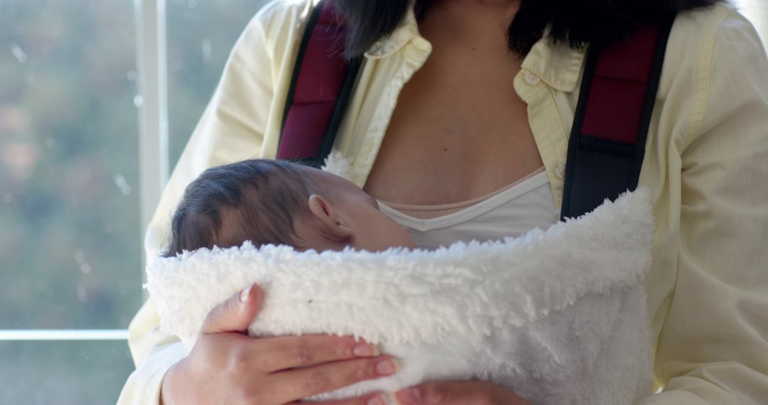 Mother Holding Newborn in Plush Carrier by Window